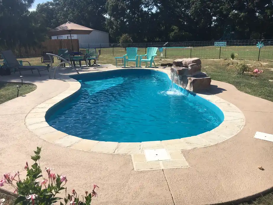 A new fiberglass pool with a rock waterfall and a broom-finish deck
