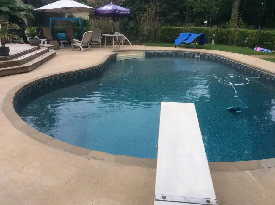 A kidney-shaped liner pool with a diving board and a textured deck