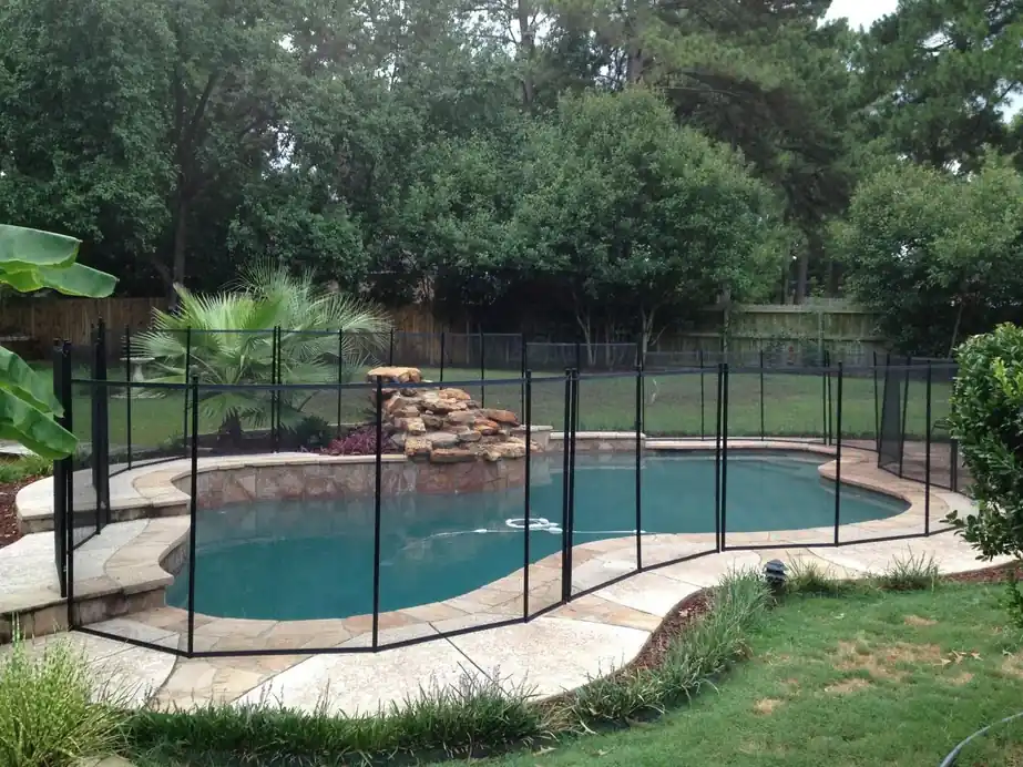 A free-form pool ringed by a black removable mesh safety fence