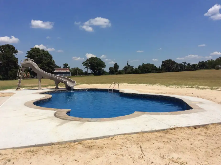 A free-form liner pool with a curving slide in an open East Texas field