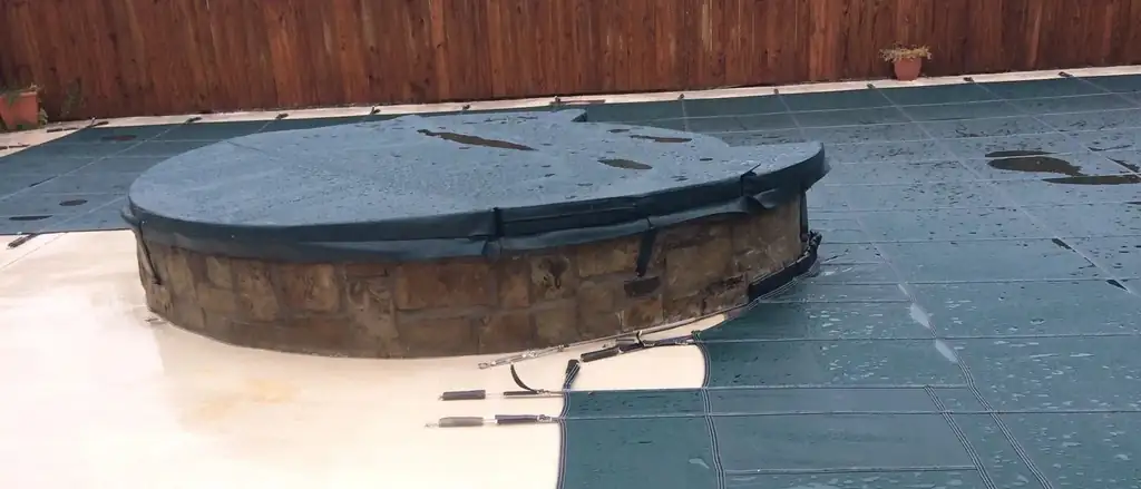 A mesh safety cover anchored over a pool and its raised stone spa